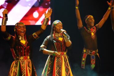 Les chanteurs du Ndlovu Youth Choir en costumes colorés sur scène, bras levés